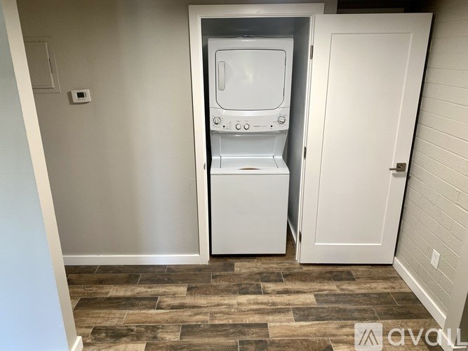 A white mini fridge is in a corner of a room with a white door and a wooden floor.