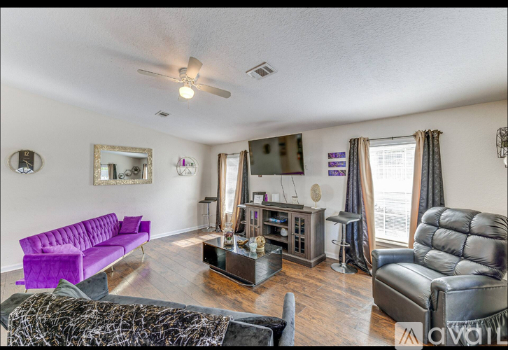 A living room with a purple couch and a black leather chair.