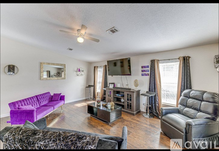 A living room with a purple couch and a black leather chair.