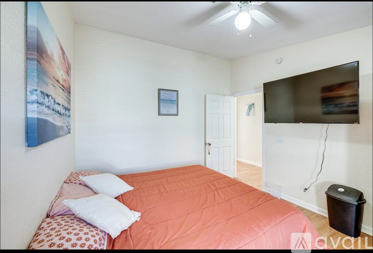 A bedroom with a bed, a ceiling fan, and a painting on the wall.