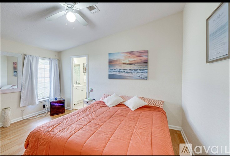 A bedroom with a bed, a ceiling fan, and a painting on the wall.