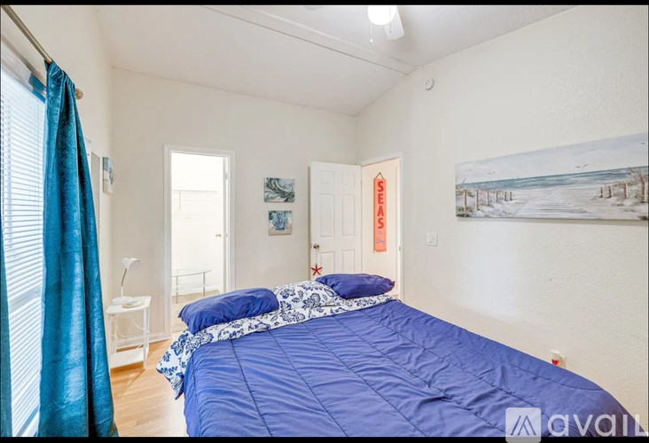 A bedroom with a blue bedspread and a white nightstand with a lamp.