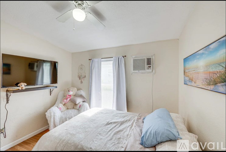 A bedroom with a bed, a ceiling fan, a window with curtains, and a painting on the wall.