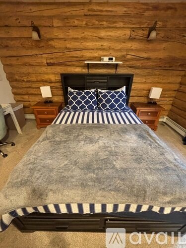 A bed with a wooden headboard and striped bedspread is in a room with a wooden wall.