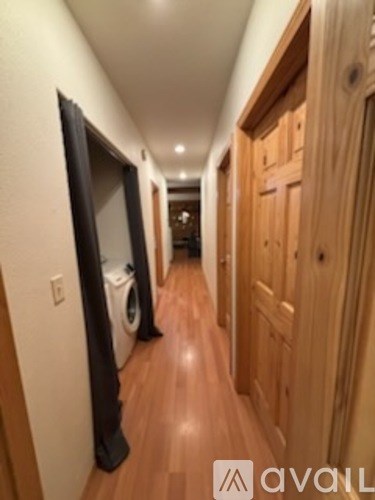 A long hallway with wood floors and a washer and dryer in the corner.