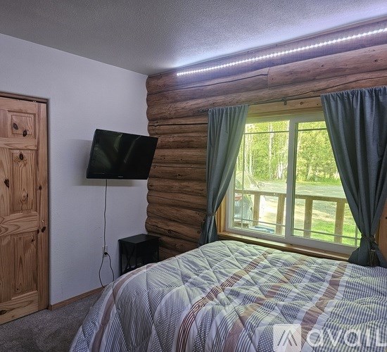 A bedroom with a bed, a television, and a window with curtains.