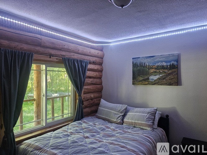 A bedroom with a bed, a window with curtains, and a painting on the wall.