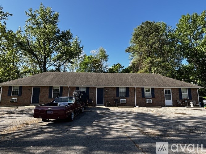 A red car is parked in front of a house with a thatched roof.