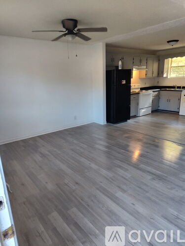 A room with a ceiling fan and a kitchen in the background.