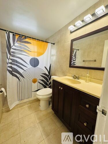 A bathroom with a toilet, sink, and a shower curtain with a leaf pattern.