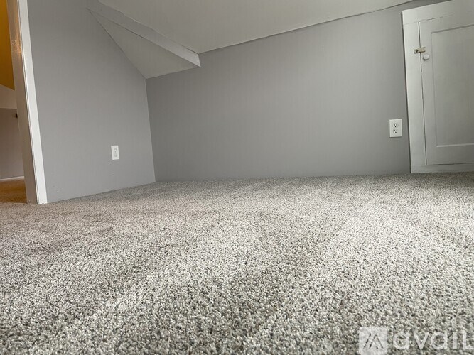 A carpeted room with a door and a light switch on the wall.