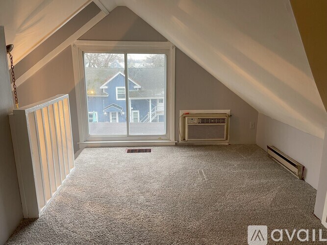 A carpeted room with a window and a view of a blue house across the way.