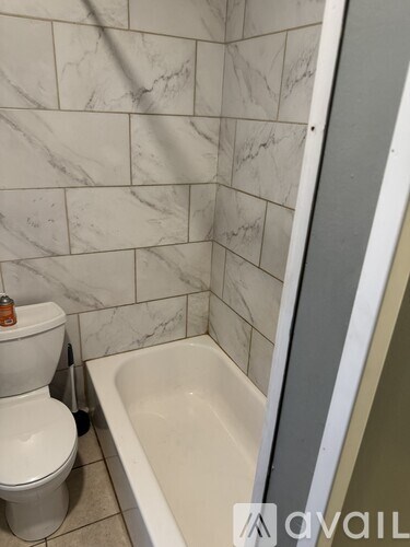 A white toilet sits next to a bathtub in a bathroom with marble tile walls.