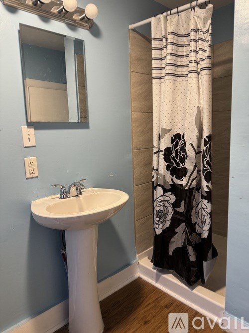 A bathroom with a white pedestal sink and a shower curtain with a floral pattern.