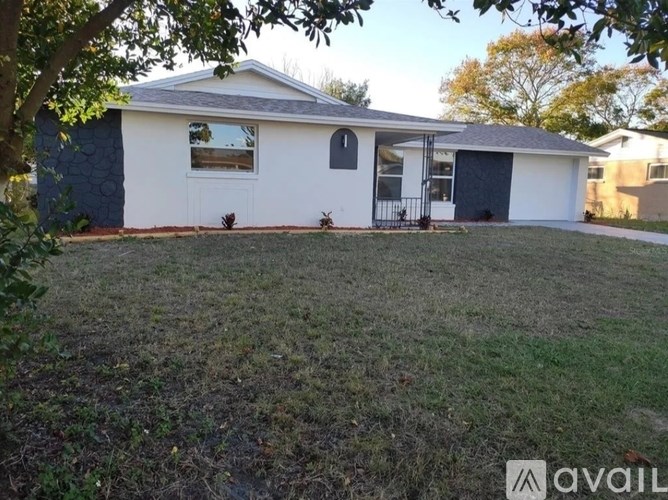 A house with a white exterior and a grey roof is surrounded by a grassy area.