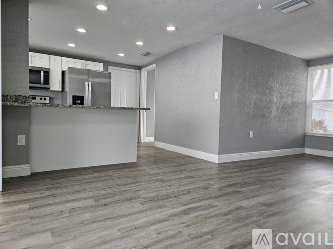 A spacious living room with a kitchen area in the background.