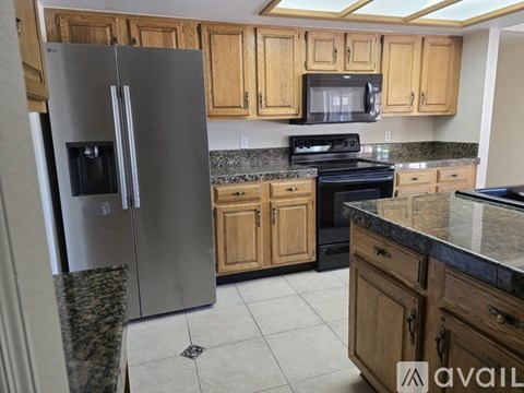 A kitchen with a stainless steel refrigerator, wooden cabinets, and granite countertops.