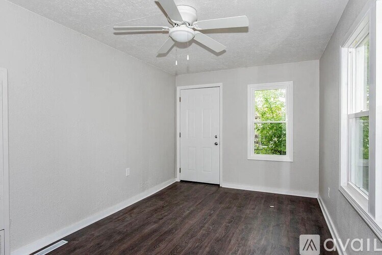 A room with a ceiling fan and a window showing greenery outside.