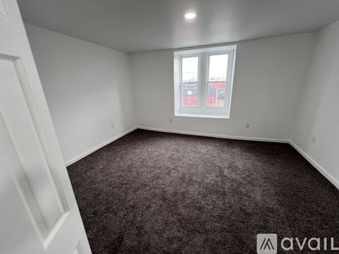 A room with a carpeted floor and a window showing a view of a street with cars and buildings.