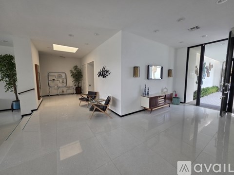A spacious living room with a white floor and walls, furnished with a sofa, chairs, and a TV.