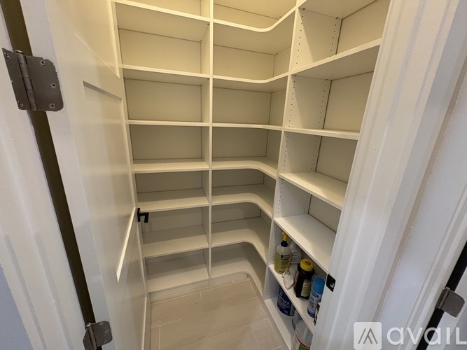 A white pantry with shelves and a few bottles on the bottom shelf.