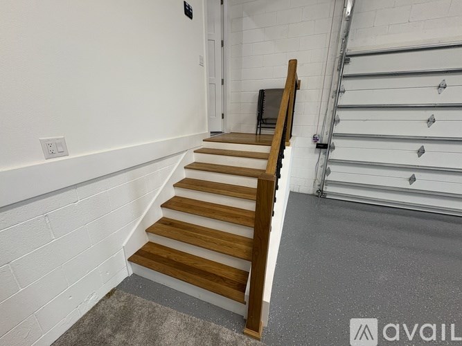 A set of wooden stairs with a white wall and a metal railing.