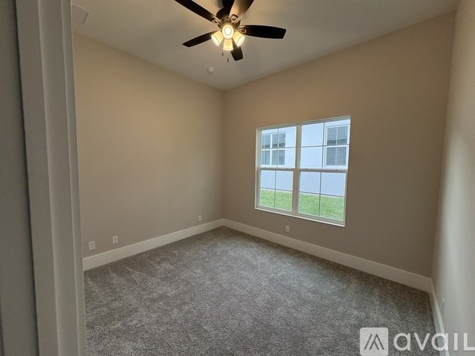 A room with a ceiling fan and a window overlooking a green area.