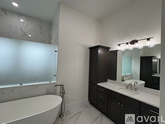A bathroom with a white tub and black cabinets.