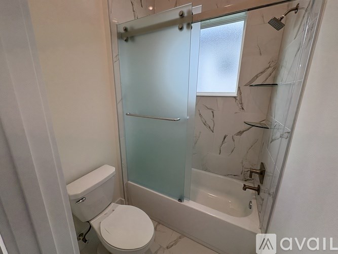 A bathroom with a toilet, a glass shower door, and a marble wall.