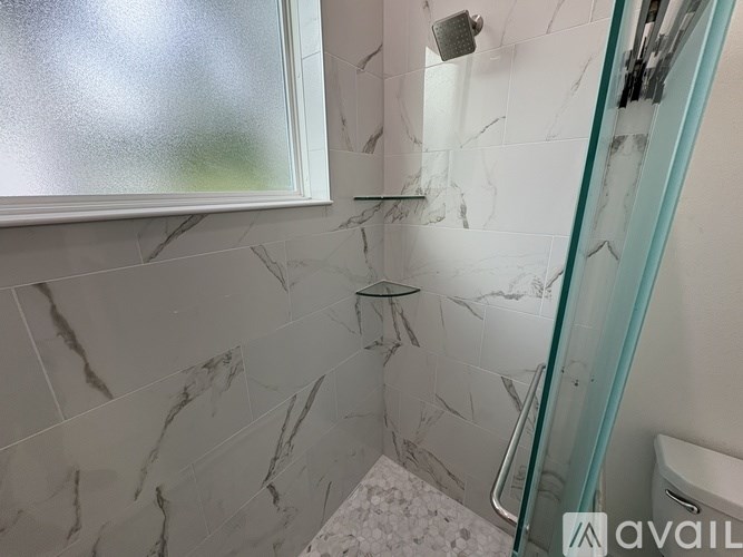 A bathroom with a marble tile wall and a glass shower door.