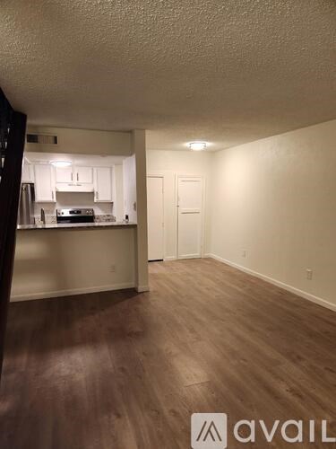 A room with wooden floors and a kitchen area in the background.