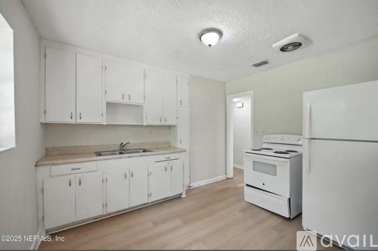A white kitchen with a sink, cabinets, and a refrigerator.