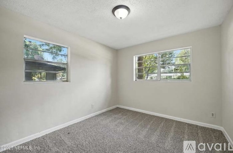 A room with a carpeted floor and two windows.