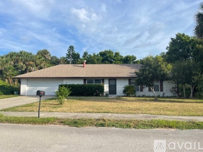 A house with a white exterior and a brown roof is surrounded by greenery.