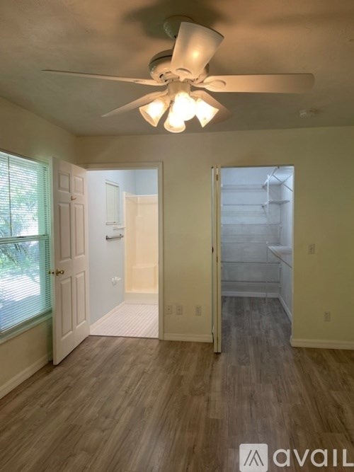 A room with a ceiling fan and light fixture, wooden flooring, and a window with blinds.