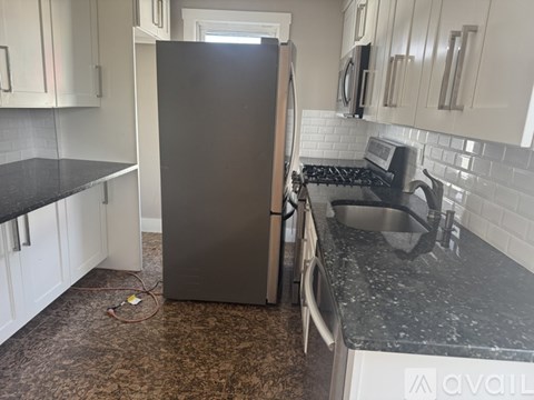 A black refrigerator in a kitchen with white cabinets.