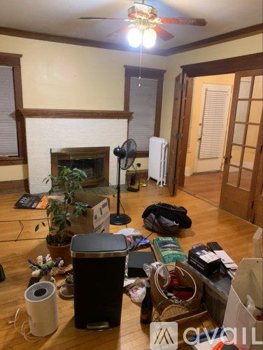 A messy room with a fireplace and a ceiling fan.