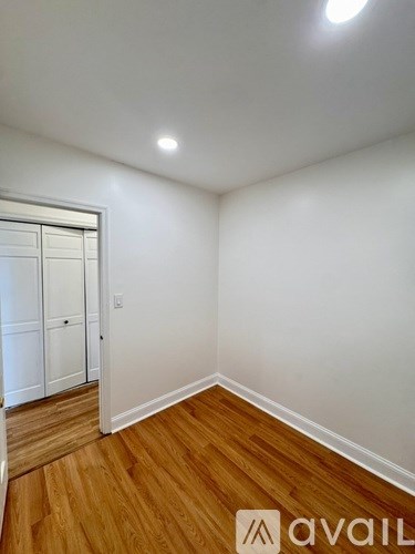 A room with wooden floors and white walls, with a door on the left side.