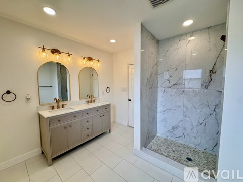 A bathroom with a marble shower and a vanity with two sinks.