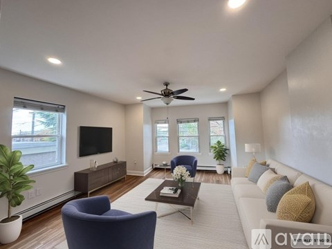 A living room with a blue armchair, a white couch, a coffee table, and a flat-screen TV.