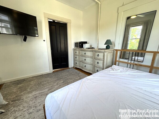 A bedroom with a large bed, a TV, a dresser, and a window.