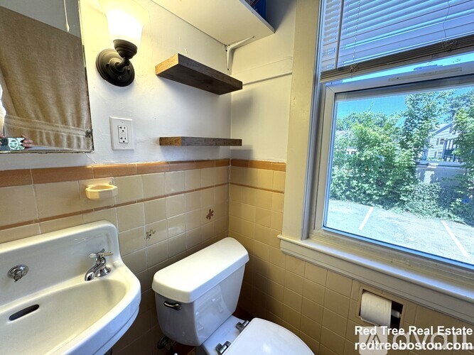 A bathroom with a toilet, sink, and window.