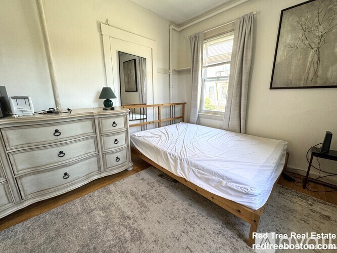 A bedroom with a bed, dresser, and window.