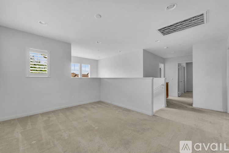 A spacious room with a carpeted floor and a window showing a view of trees and houses outside.