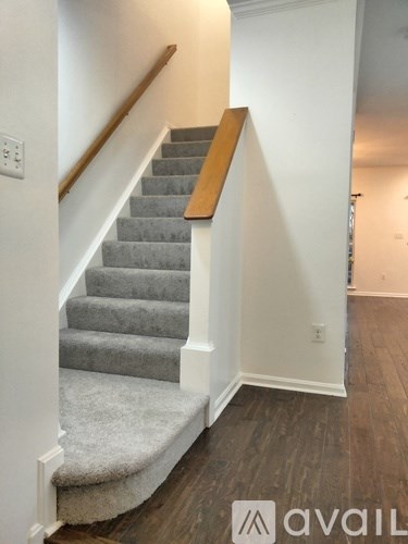 A staircase with a wooden handrail and grey carpeted steps.