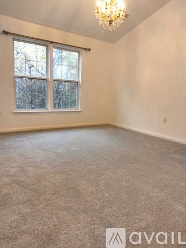 A room with a carpeted floor, a window with a view of trees, and a chandelier hanging from the ceiling.