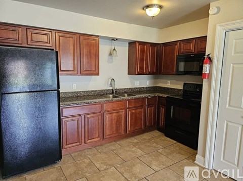 A kitchen with brown cabinets and a black refrigerator.