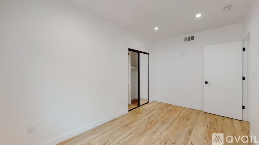 A room with a white wall and a wooden floor with a door on the left side.