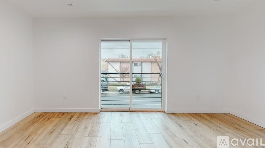 A room with wooden flooring and a large window with a view of a street and buildings outside.