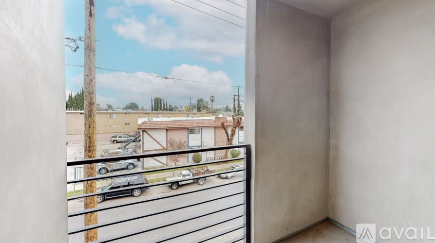 A balcony with a metal railing overlooks a street with parked cars and buildings.